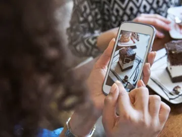 A woman at a table with two other restaurant guests uses her mobile phone to take a photo of a chocolate dessert.